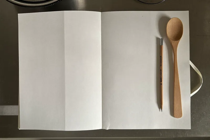 A notebook and pencil beside a wooden spoon on a kitchen counter